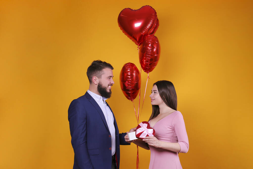Gelukkige Valentijnsdag concept. Studio shot van een verliefd stel met een hartvormige ballon. Portret van een man met baard en een meisje in roze jurk poserend over een gele muurachtergrond. Kopieer ruimte, casual stijl - Foto, afbeelding