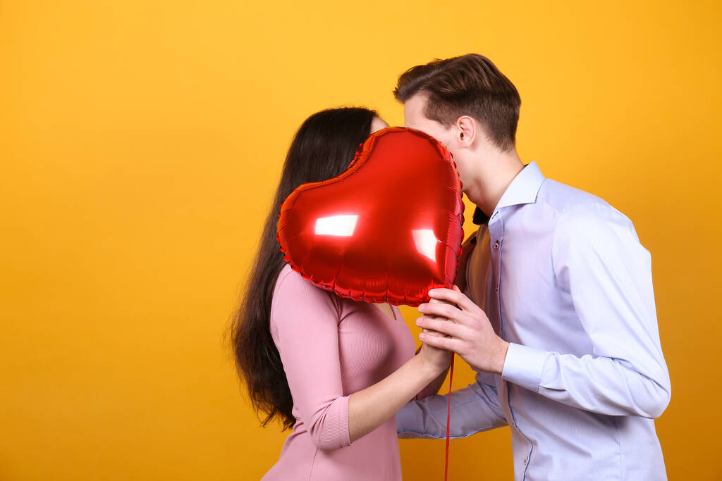 Wesołych Walentynek. Studyjne ujęcie zakochanej pary trzymającej balon w kształcie serca, okazujące uczucie. 14 lutego - dzień kochanków. Żółta ściana tło, przestrzeń do kopiowania, widok z przodu portret. - Zdjęcie, obraz