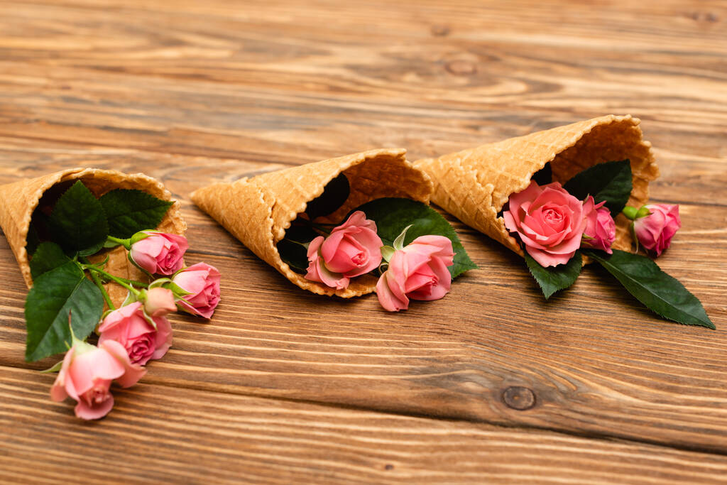 рожеві чайні троянди в вафельних конусах на дерев'яній поверхні
 - Фото, зображення