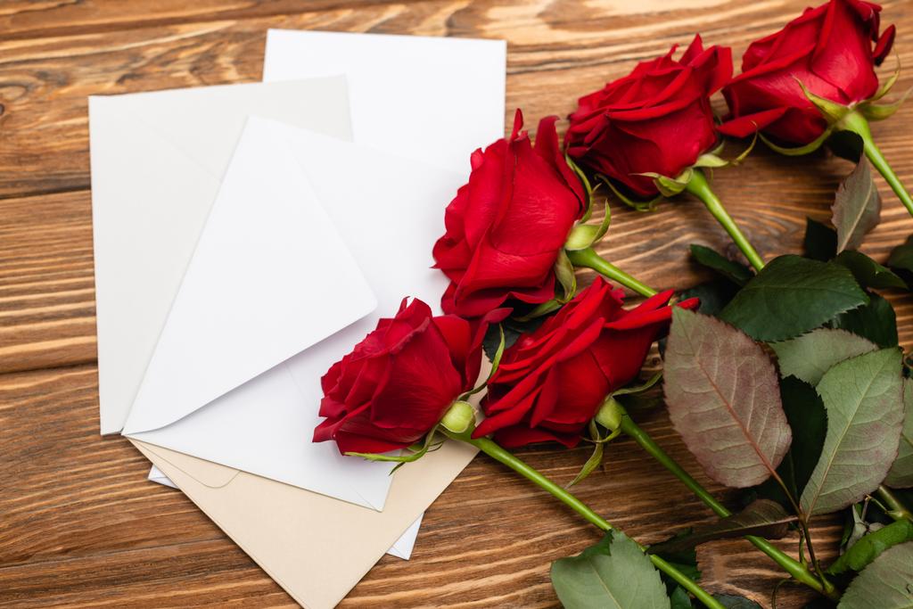 Hochwinkelaufnahme von Rosen in der Nähe von Briefumschlägen und Papieren auf Holzoberfläche  - Foto, Bild