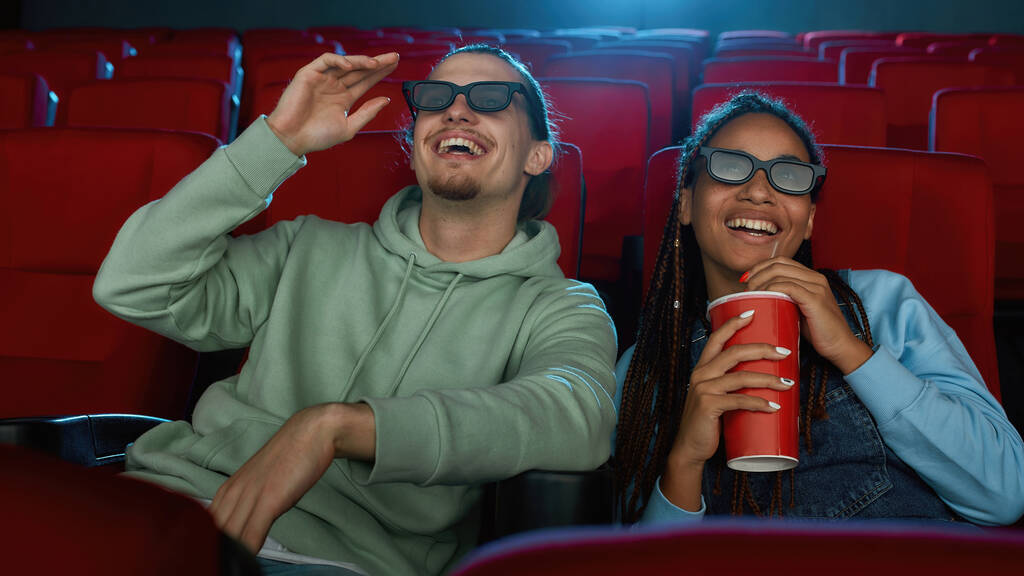 Πορτρέτο του χαρούμενου νεαρού ζευγαριού φορώντας 3d γυαλιά χαμογελώντας ενώ παρακολουθείτε μια ταινία μαζί στο αμφιθέατρο κινηματογράφου και πίνοντας σόδα - Φωτογραφία, εικόνα