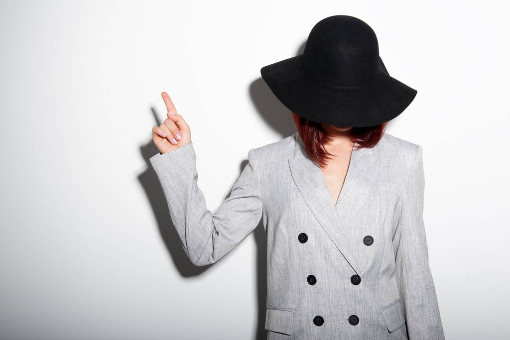Mysterieuze mode jonge vrouw in zwarte hoed wijzend op kopieerruimte waar kan de reclameboodschap worden geschreven - Foto, afbeelding