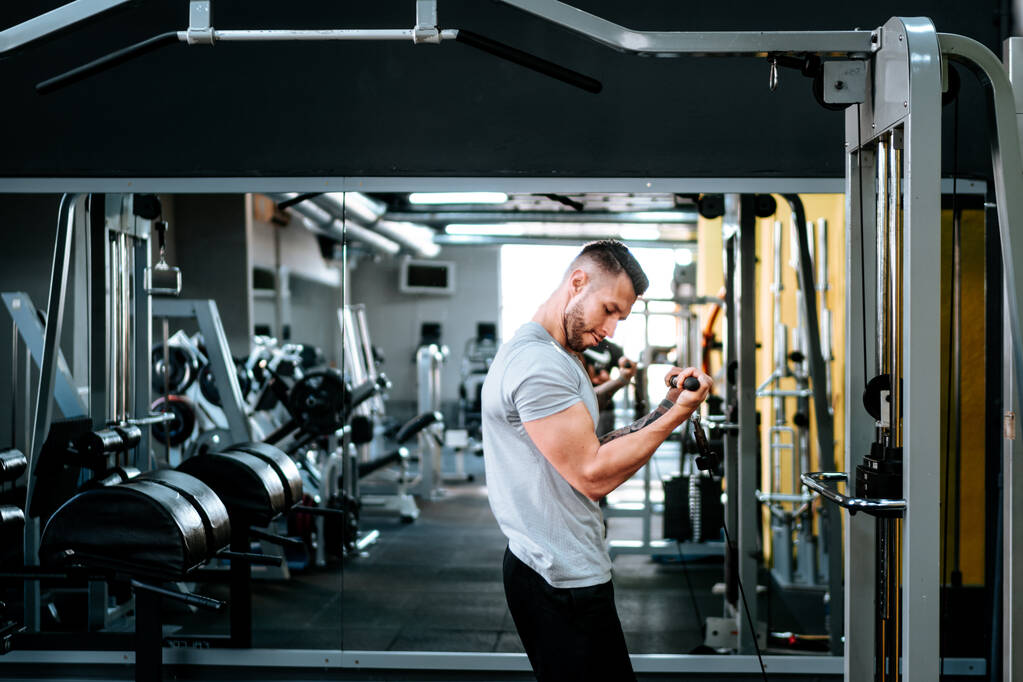 Мускулистый мужчина тренирует руки и бицепсы в спортзале. Концепция здорового образа жизни - Фото, изображение