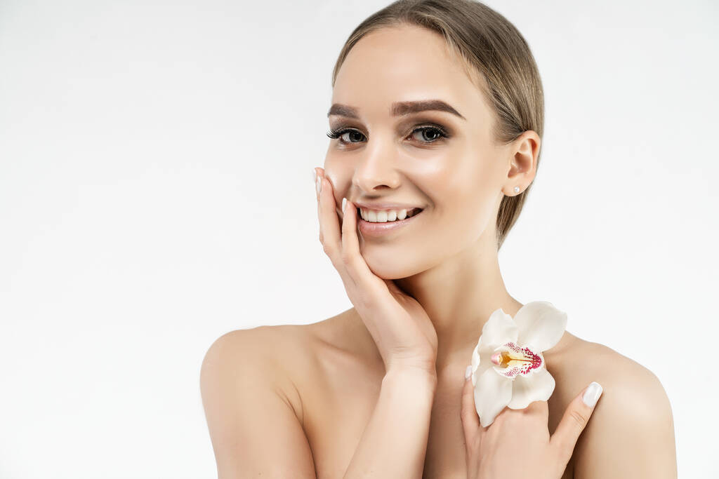 Refresh, beauty and health. Portrait of a beautiful woman holding a hand near a smiling face and holding an orchid with the other hand. Spa center. Place for text. - Foto, afbeelding