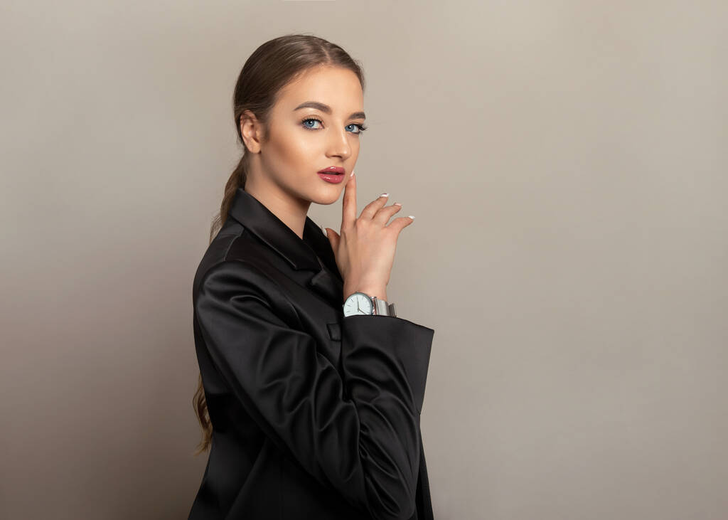 Красивая молодая женщина со здоровой и сияющей кожей, позирующая в черном пиджаке и носящая девчачьи часы - Фото, изображение