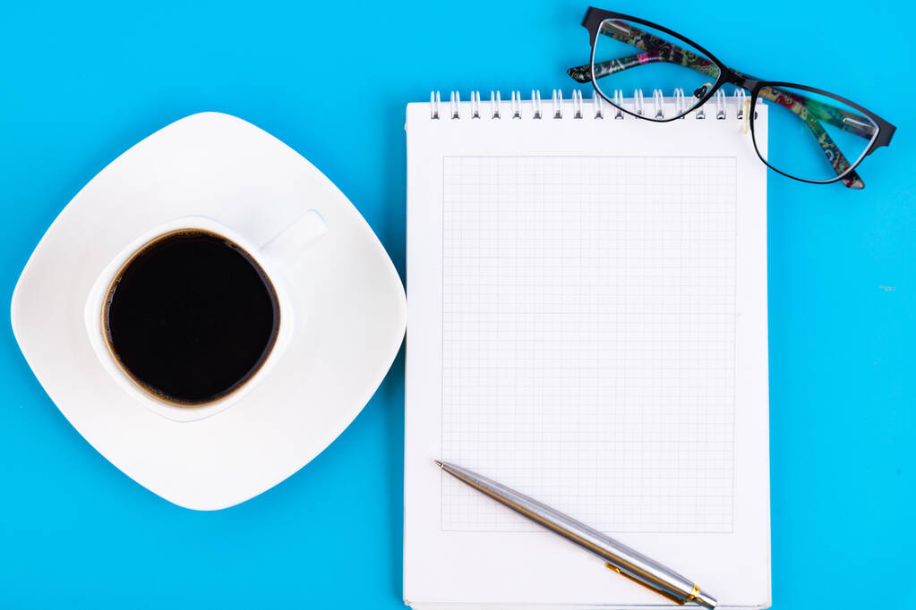 Leeres weißes Notizbuch, mit Stift, Brille und einer Tasse Kaffee auf einem blauen Tisch. Geschäftskonzept. - Foto, Bild