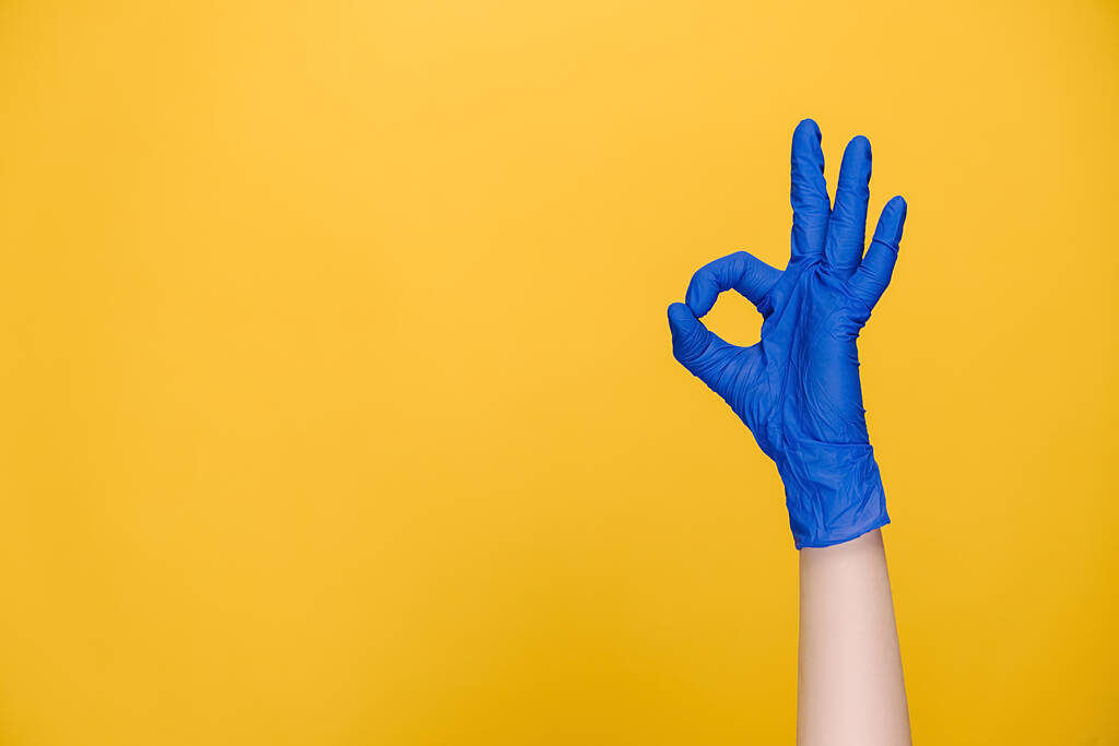 医療用保護手袋の男性の手の閉鎖は、コピースペースと黄色のスタジオの背景に隔離されたokのサインを実証し、お祝いと勝利を表現しています。ボディランゲージの概念。手札 - 写真・画像