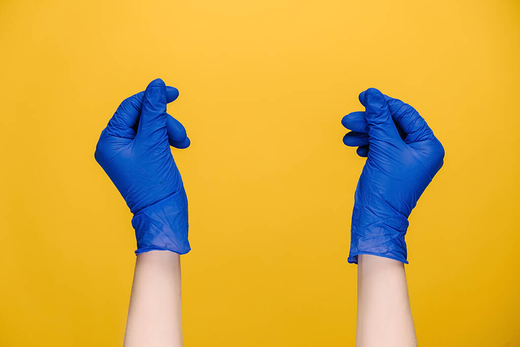 Zbliżenie męskich rąk w medycznych rękawiczkach ochronnych pocierających palce pokazując gest gotówki prosząc o pieniądze, izolowane na żółtym tle studio z miejsca na reklamę. Pojęcie języka ciała - Zdjęcie, obraz