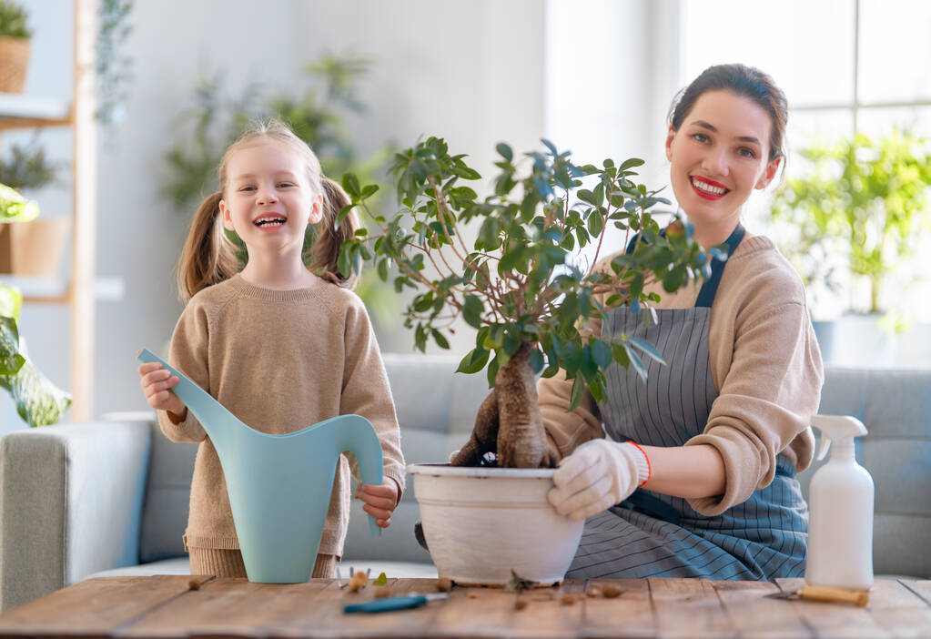 Cute dziewczynka pomaga matce dbać o rośliny. Mama i jej córka zajmują się ogrodnictwem w domu. Szczęśliwa rodzina w wiosenny dzień. - Zdjęcie, obraz