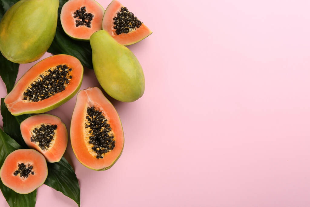 Fruits frais de papaye mûrs avec des feuilles vertes sur fond rose, plat. Espace pour le texte - Photo, image