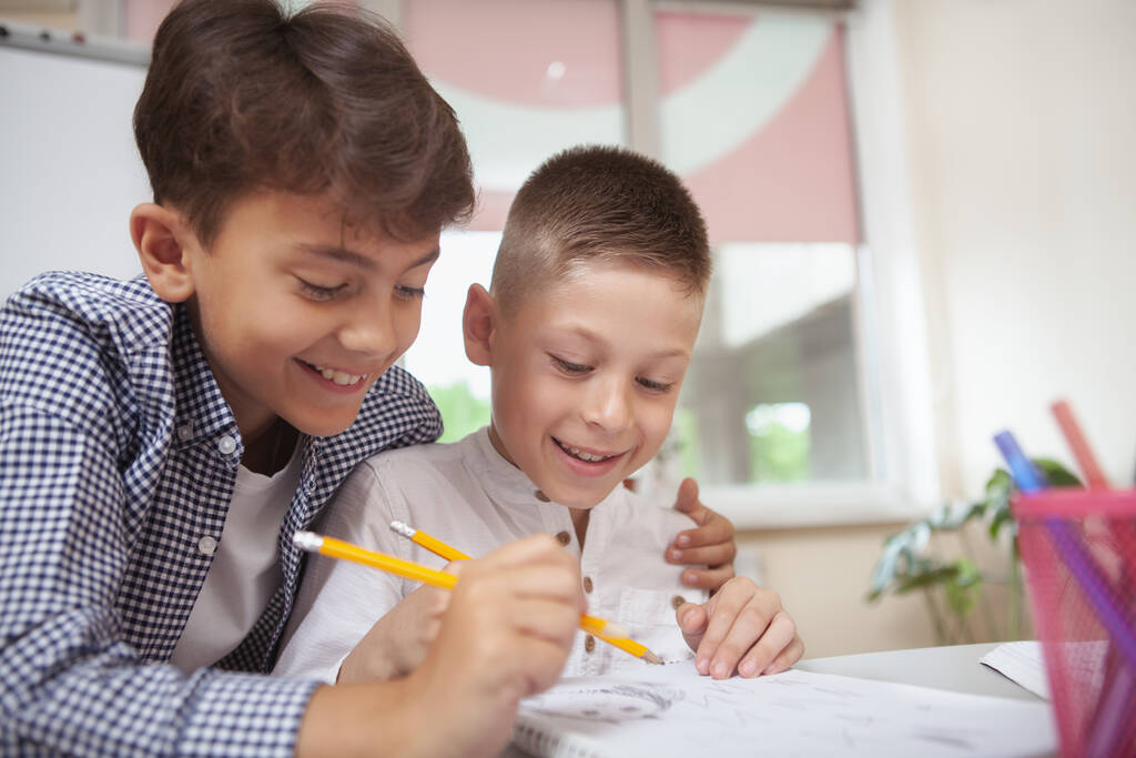 Gelukkige jonge jongens die praten en lachen terwijl ze samen tekenen in de klas, kopiëren ruimte. CHarming basisschool leerlingen concentreren, werken aan kunst project samen - Foto, afbeelding