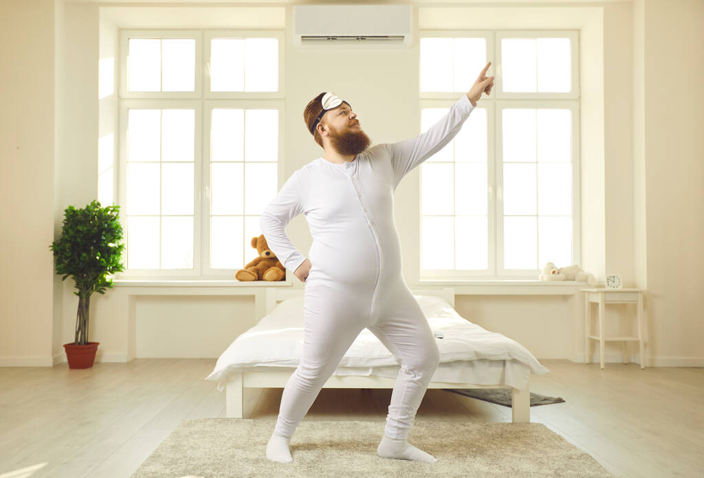 Cheerful chubby young man in pajamas dancing in light sunny bedroom in the morning - Photo, Image