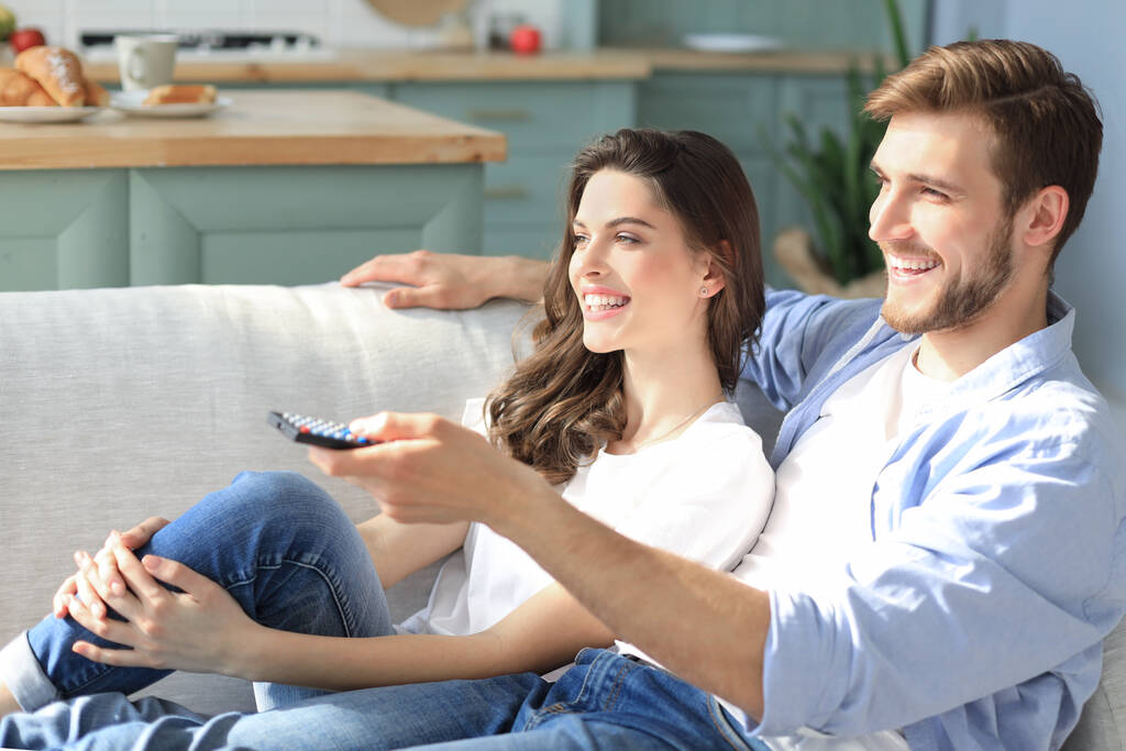 Jovem casal amoroso no sofá em casa assistindo tv e rindo - Foto, Imagem