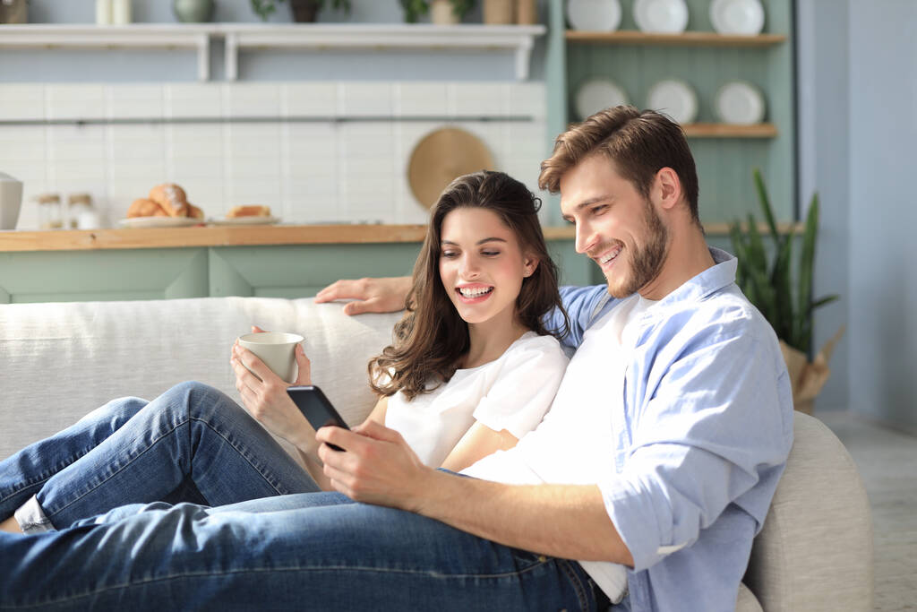 Młoda para ogląda treści online w smartfonie siedząc na kanapie w domu w salonie - Zdjęcie, obraz