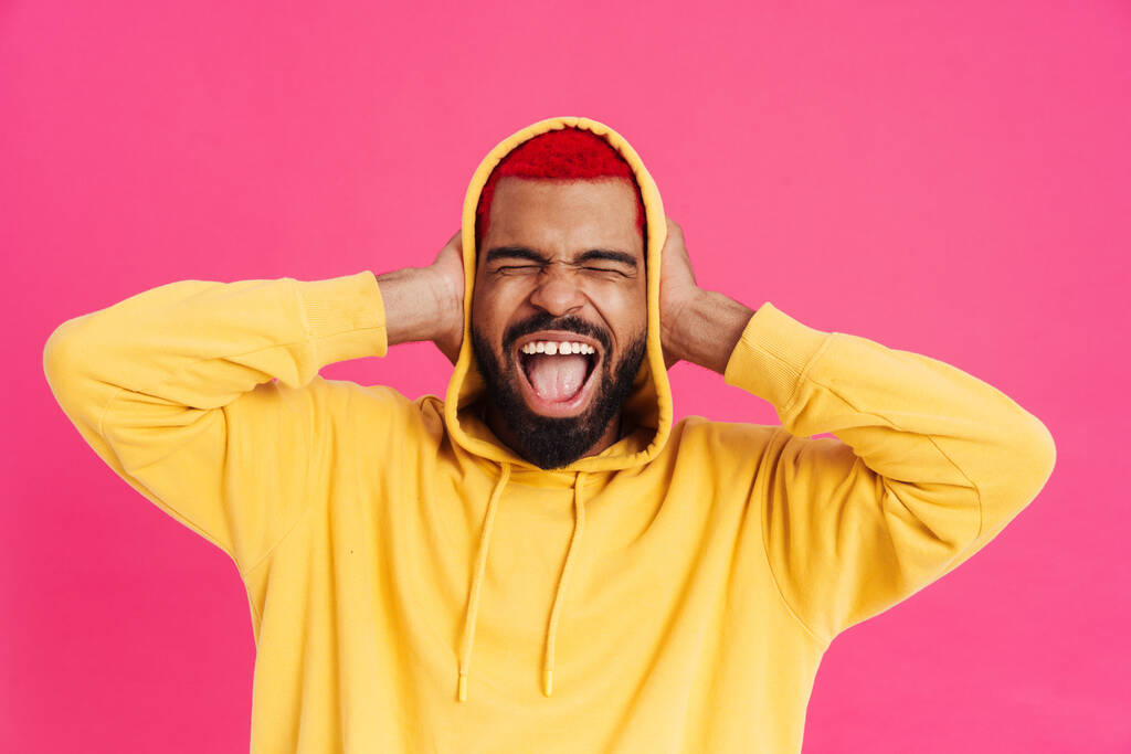 Innoissaan afrikkalainen amerikkalainen kaveri huutaa ja peittää korvansa eristetty vaaleanpunainen tausta - Valokuva, kuva