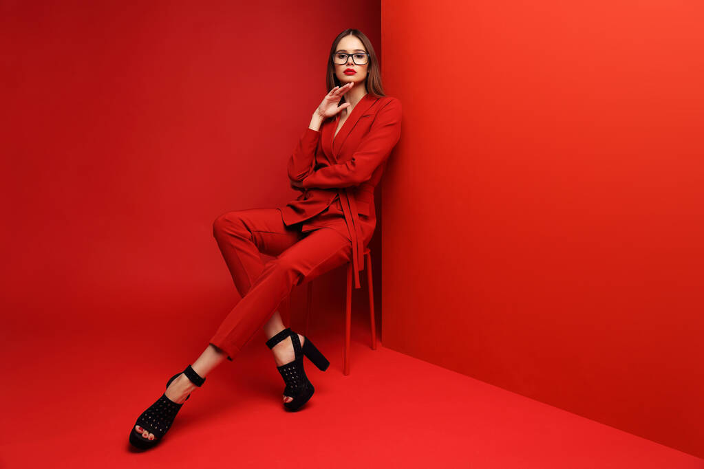 Μόδας νεαρή γυναίκα με κόκκινο κοστούμι. Κόκκινο φόντο. - Φωτογραφία, εικόνα