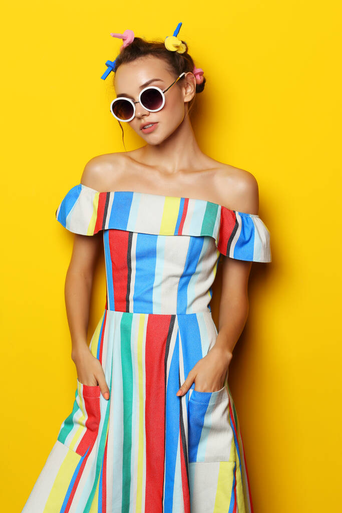 Chica cool moda posando en gafas de sol sobre fondo amarillo. Joven mujer hipster, rizadores en el pelo  - Foto, imagen