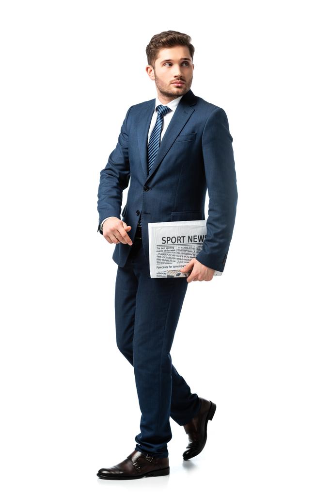 vue pleine longueur de jeune homme d'affaires regardant loin tout en marchant avec le journal sur blanc - Photo, image