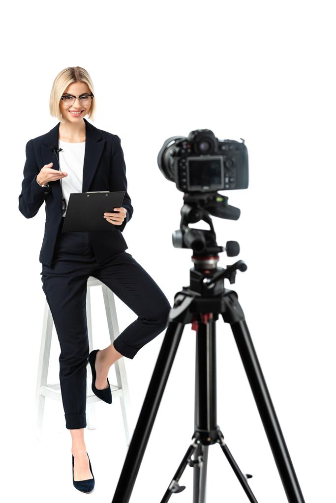 smiling broadcaster pointing at clipboard near digital camera on white, blurred foreground - Photo, Image