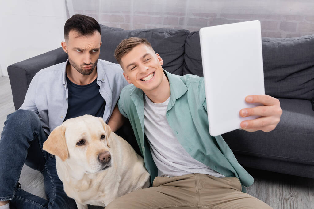szczęśliwy sam płeć para biorąc selfie na cyfrowy tablet w pobliżu labrador w salonie - Zdjęcie, obraz