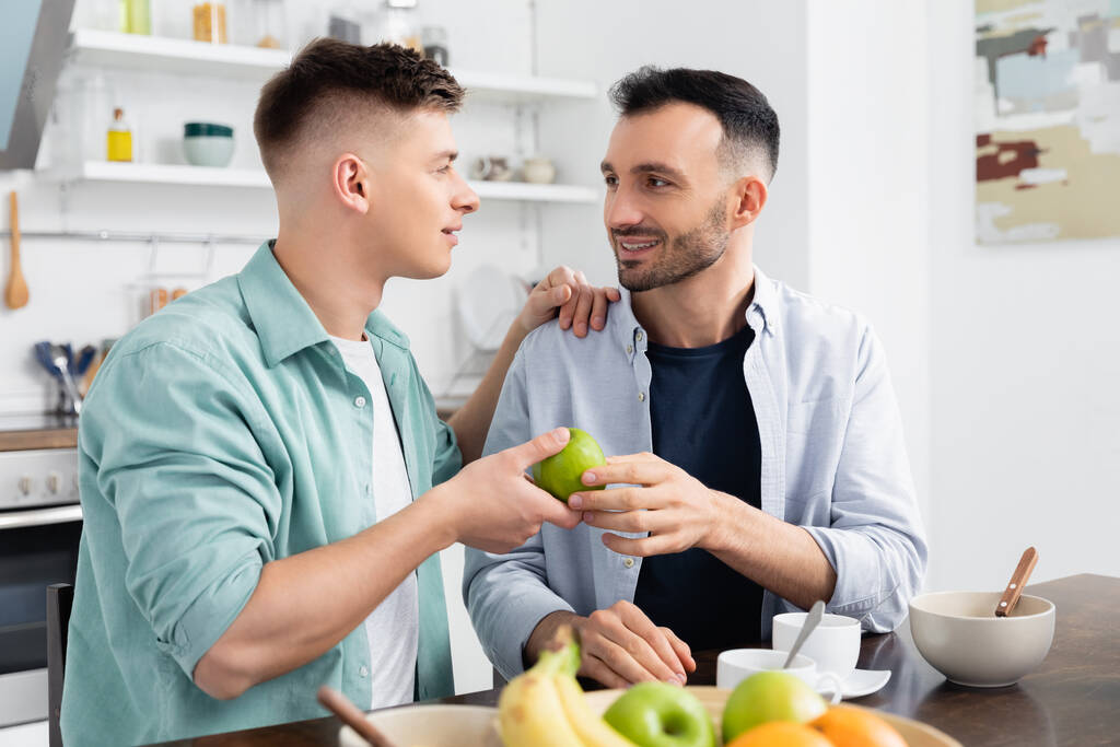 キッチンで夫にアップルを与える幸せな同性愛者の男  - 写真・画像
