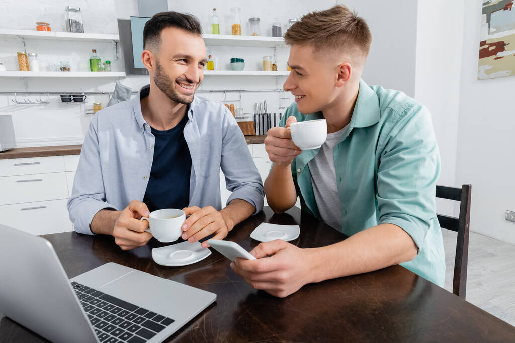 onnellinen homoseksuaali pari kahvi lähellä kannettavaa tietokonetta pöydällä - Valokuva, kuva