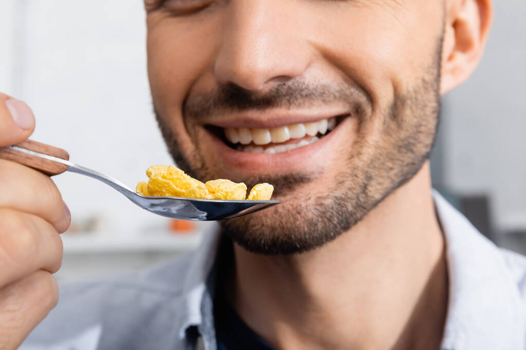 bijgesneden blik van gelukkig man houden lepel met cornflakes - Foto, afbeelding
