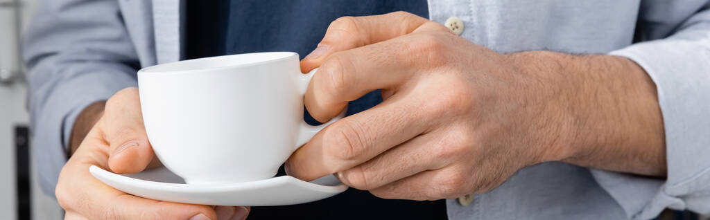 コーヒーとソーサー、バナー付きのカップを持つ男のクロップドビュー - 写真・画像