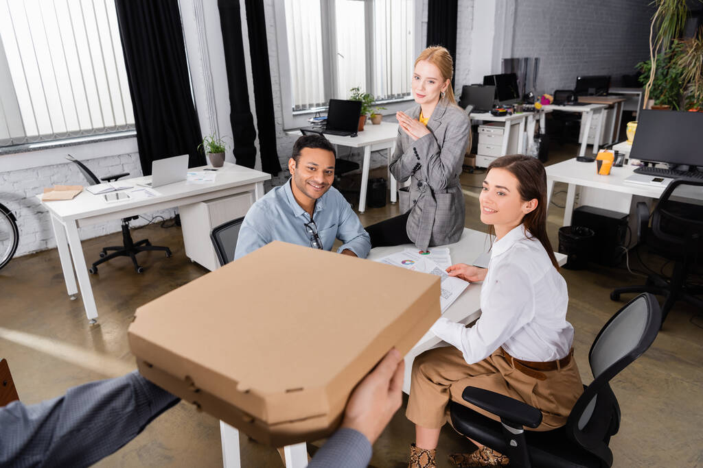 Hymyilevät monikansalliset liikemiehet katselevat pizzalaatikoiden lähettäjää hämärtyneellä etualalla  - Valokuva, kuva