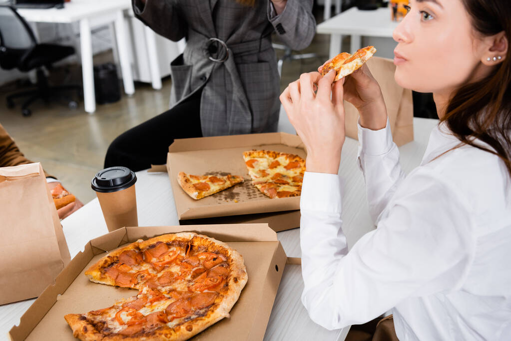 Nuori liikenainen syö pizzaa lähellä kollegoita toimistossa  - Valokuva, kuva