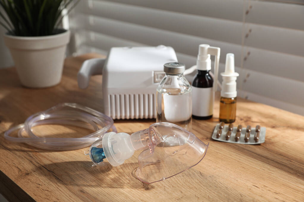 Nebulizador moderno con mascarilla facial y medicamentos en mesa de madera en interiores. Equipo de inhalación - Foto, Imagen