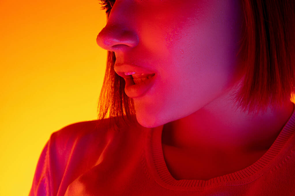 Kaukasische Frauenporträt isoliert auf orangefarbenem Studiohintergrund in buntem Neonlicht - Foto, Bild