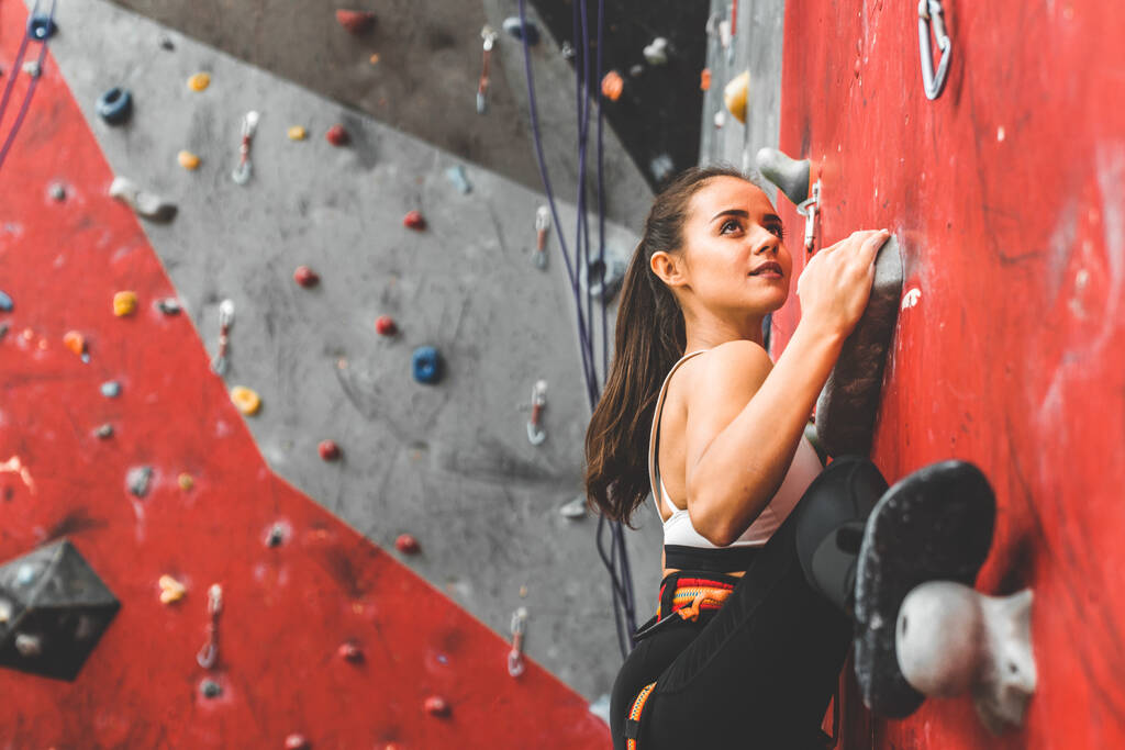 Deportiva escaladora ascendiendo sobre roca escarpada, escalando en pared artificial en interiores. Concepto de deportes extremos y bouldering - Foto, Imagen