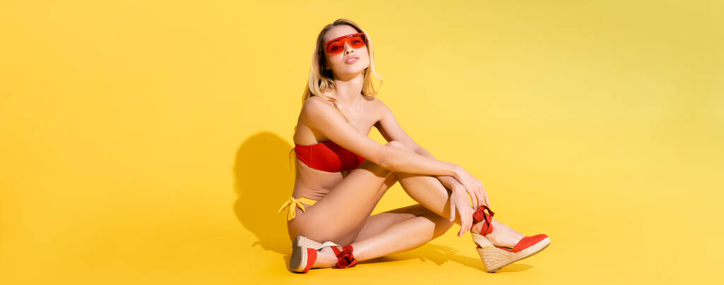 young woman in sandals and swimsuit looking at camera while posing on yellow, banner - Photo, Image
