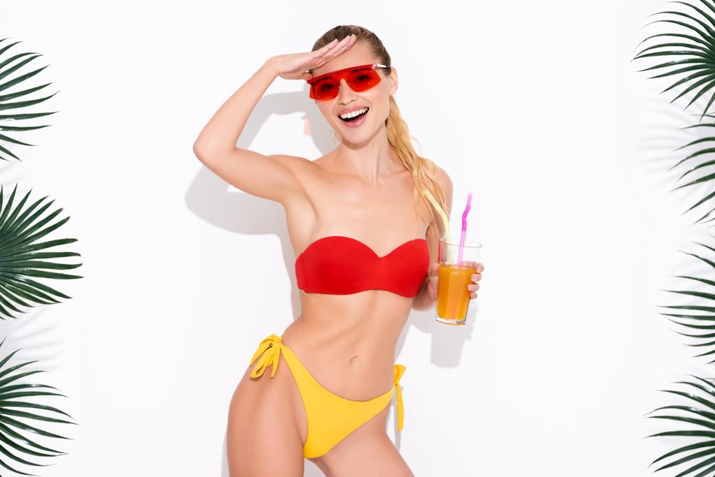 вражена жінка в купальнику і сонцезахисних окулярах дивиться на камеру, тримаючи свіжий коктейль на білому
 - Фото, зображення