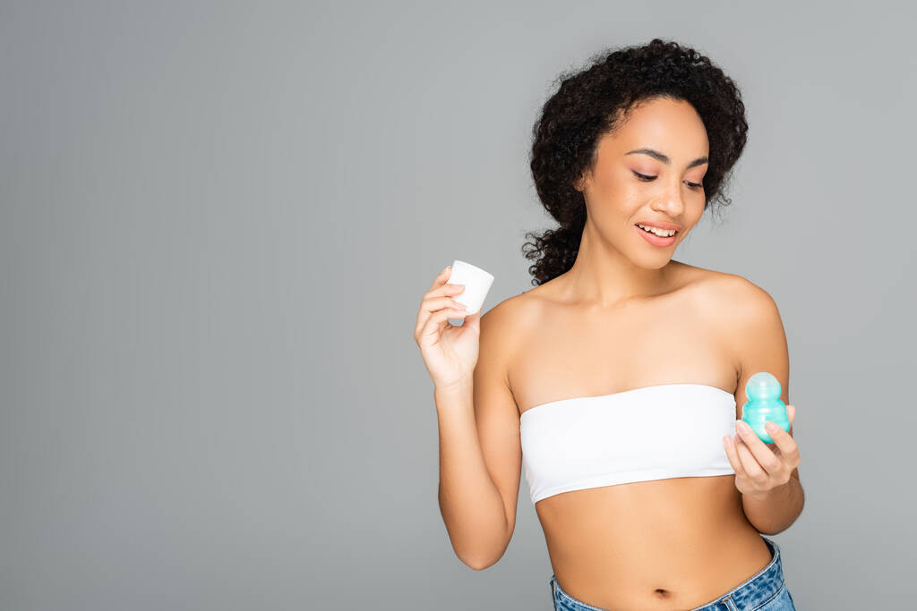 Uśmiechnięta Afroamerykanka trzymająca dezodorant na szaro  - Zdjęcie, obraz