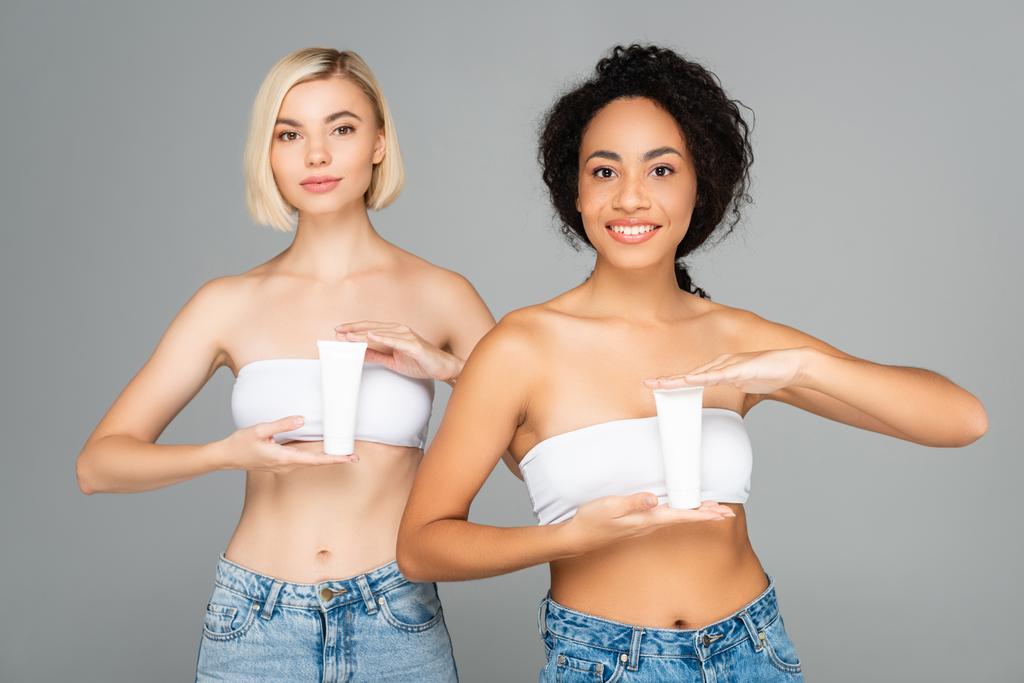 Femmes multiethniques tenant des tubes avec crème cosmétique isolée sur gris  - Photo, image