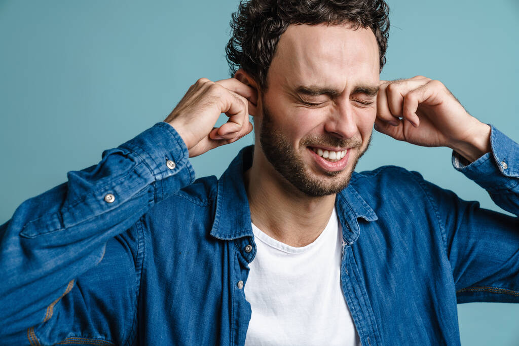 Cheerful handsome guy with eyes closed plugging his ears isolated over blue background - Photo, Image