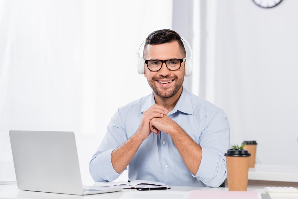 χαρούμενος επιχειρηματίας με γυαλιά και ακουστικά χαμογελώντας κοιτάζοντας την κάμερα - Φωτογραφία, εικόνα