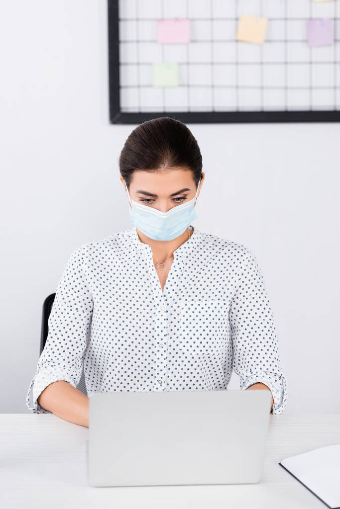 femme d'affaires en masque médical à l'aide d'un ordinateur portable au bureau - Photo, image