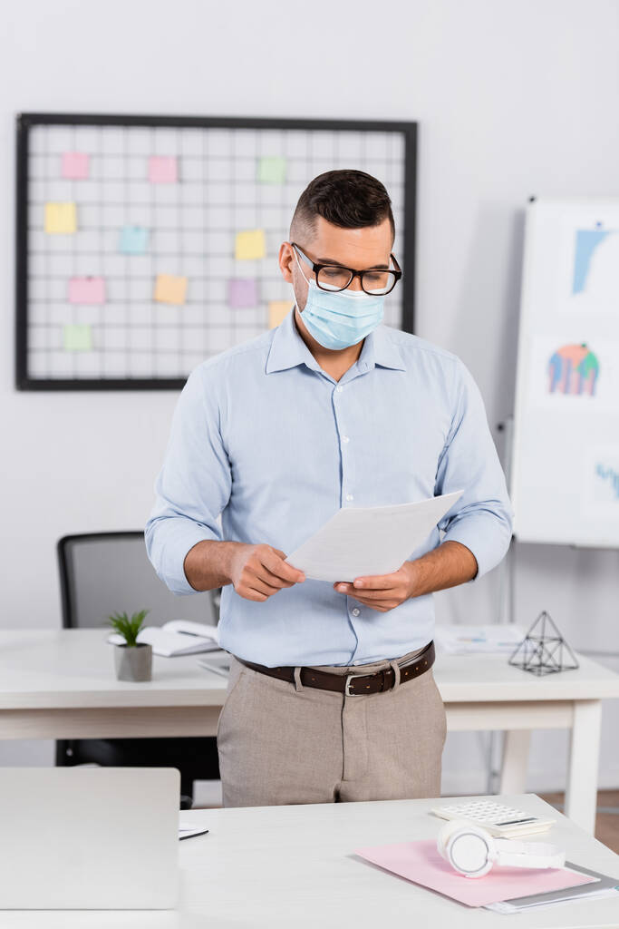Geschäftsmann mit medizinischer Maske und Brille schaut sich Dokumente an - Foto, Bild