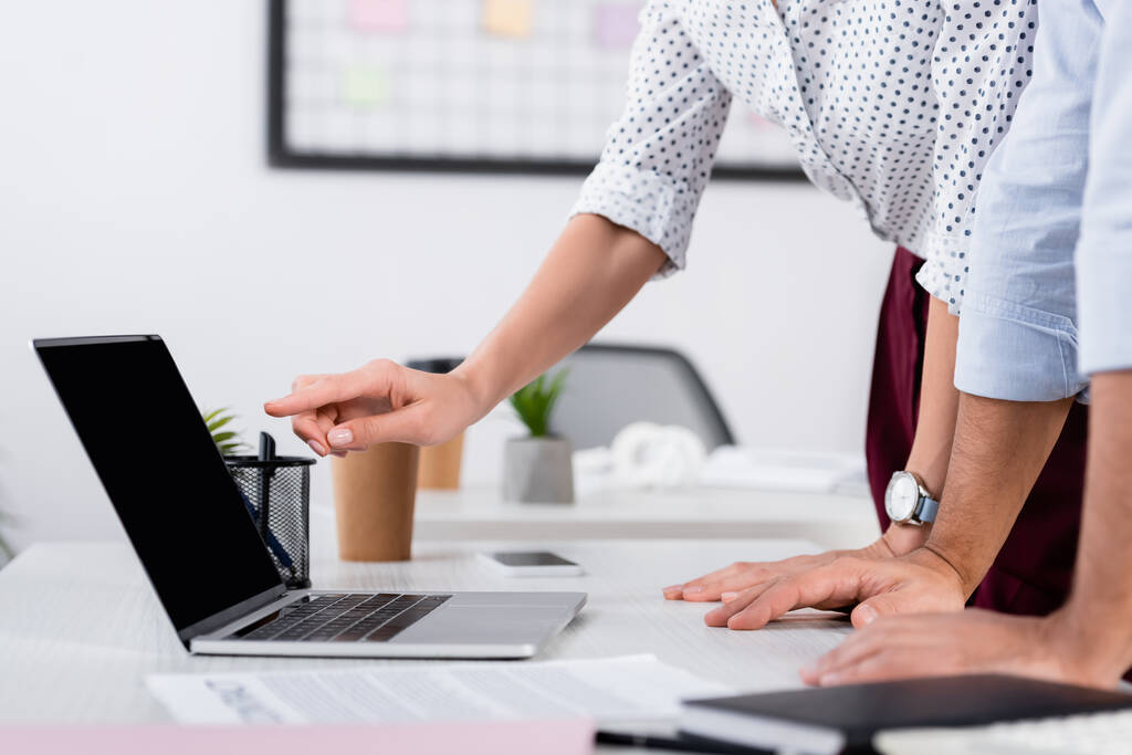 Ausgeschnittene Ansicht einer Geschäftsfrau, die mit dem Finger auf Laptop mit leerem Bildschirm auf Schreibtisch zeigt - Foto, Bild