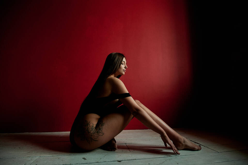 Portret van een tattoo vrouw in een zwart pak zittend op de studio vloer. Modeconcept - Foto, afbeelding