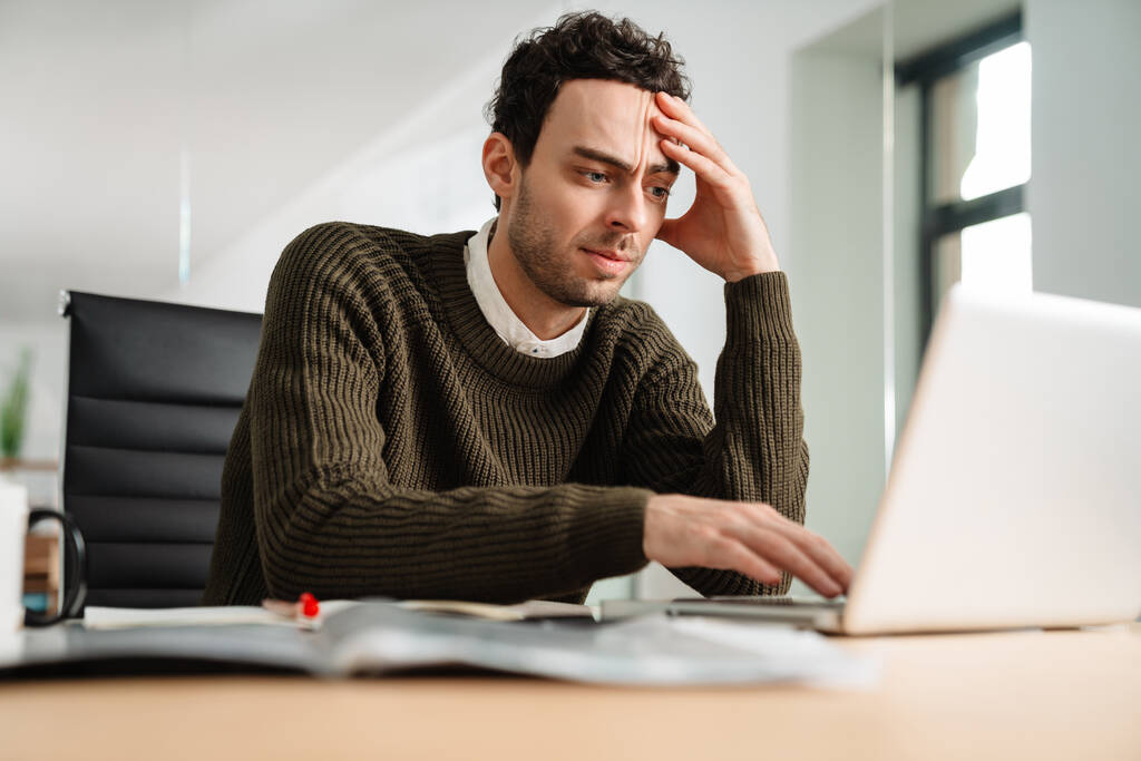 Στρεσαρισμένος επιχειρηματίας κοιτάζοντας φορητό υπολογιστή, ενώ κάθεται στο γραφείο - Φωτογραφία, εικόνα