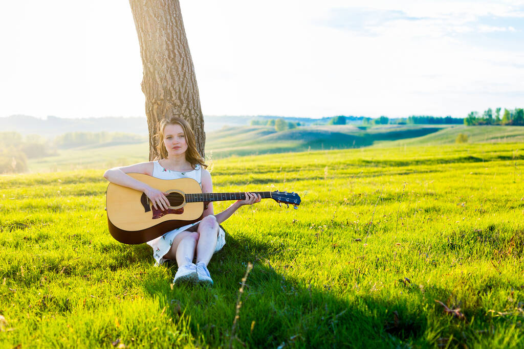 少女はフィールドでアコースティックギターで座っている碑文のためのコピースペース - 写真・画像
