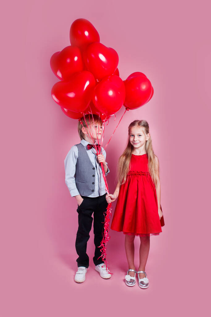 バレンタインデー。ピンクの背景にハート型の気球を持つ2人の幸せな子供。初恋 - 写真・画像