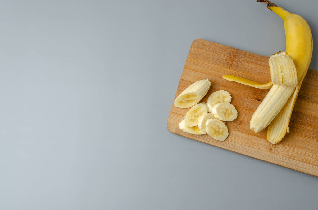 Gesneden banaan op hout snijplank op een grijze achtergrond. Trending kleur Pantone van jaar 2021 Verhelderend en Ultimate grijs. Top view minimale stilleven met kopieerruimte. - Foto, afbeelding