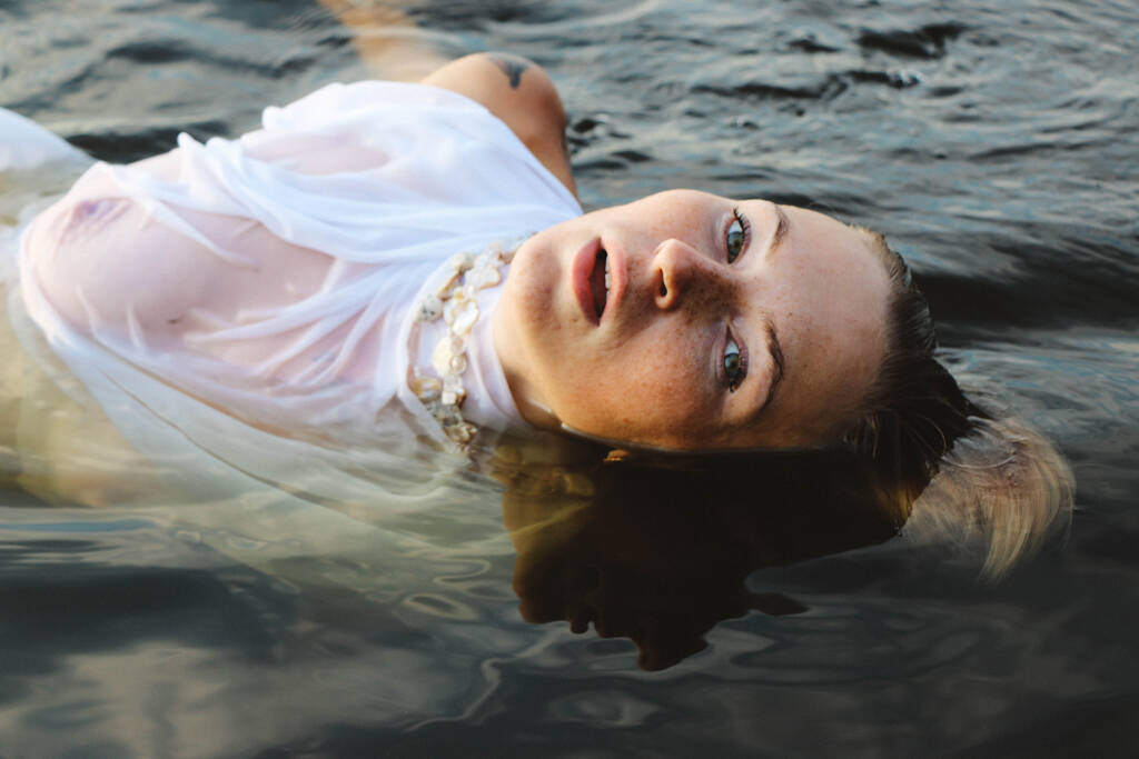 portré egy gyönyörű fiatal nőről a vízben, szeplőkkel és zöld szemekkel. Gyönyörű naplemente fény. atlétikai test, közel a tó, a háttérben a víz - Fotó, kép