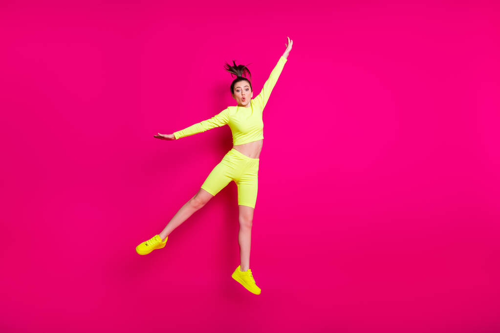 Teljes hossz testméret fotó ugrás magas fiatal sportos nő visel sárga sportruházat tornacipő elszigetelt élénk rózsaszín háttér - Fotó, kép