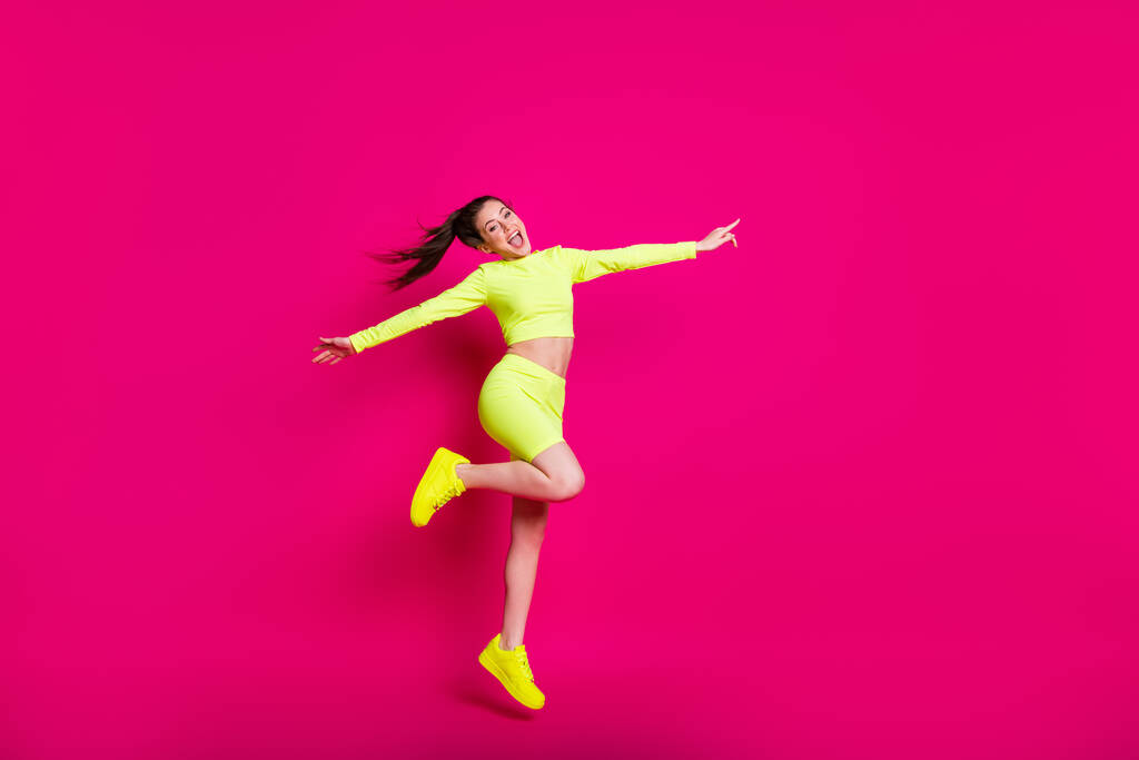 Pleine longueur taille du corps photo de sportif sautant riant pointant joyeusement vers copyspace isolé sur fond de couleur rose vif - Photo, image